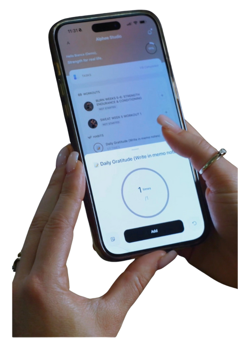 A person holding a smartphone with a finger touching the screen, showing Alphee Studio app interface. The phone is isolated on a solid black background.